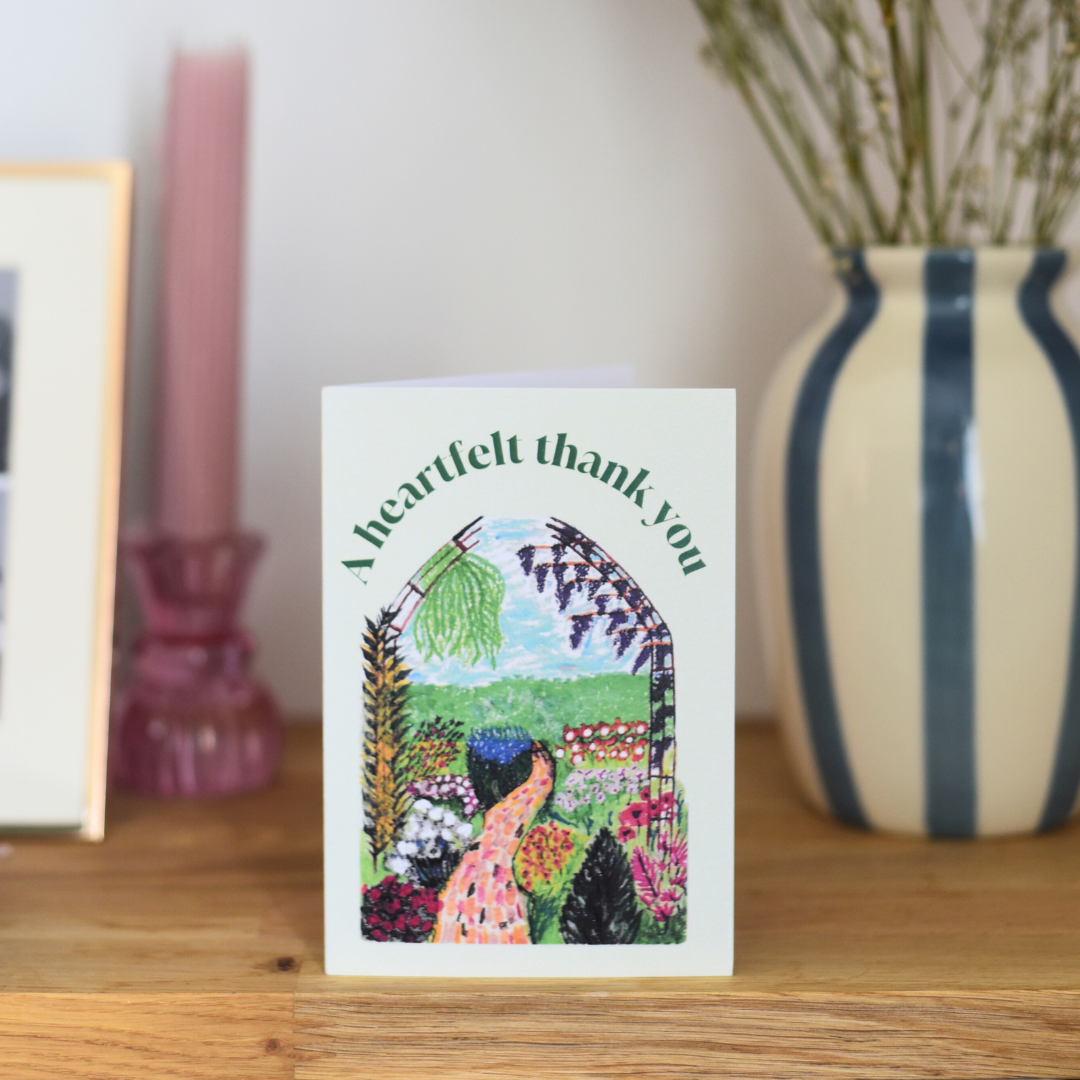 Greeting card with garden design and 'A heartfelt thank you' text on a wooden surface with decor items.