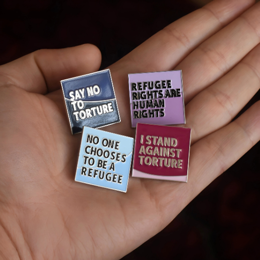 Four protest pins held in a hand, with messages about human rights and refugees.