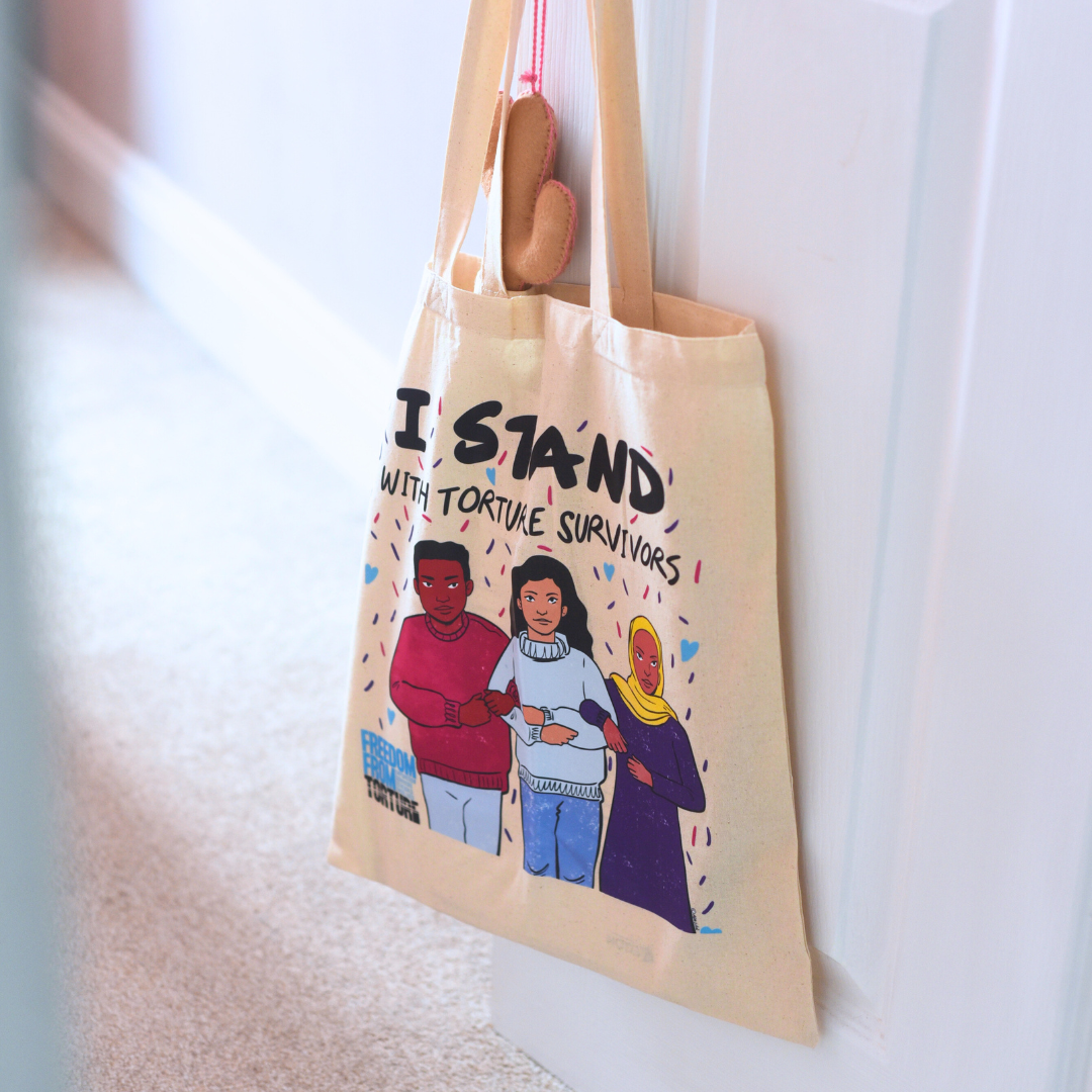 Beige tote bag with illustrations and text on a white wall background