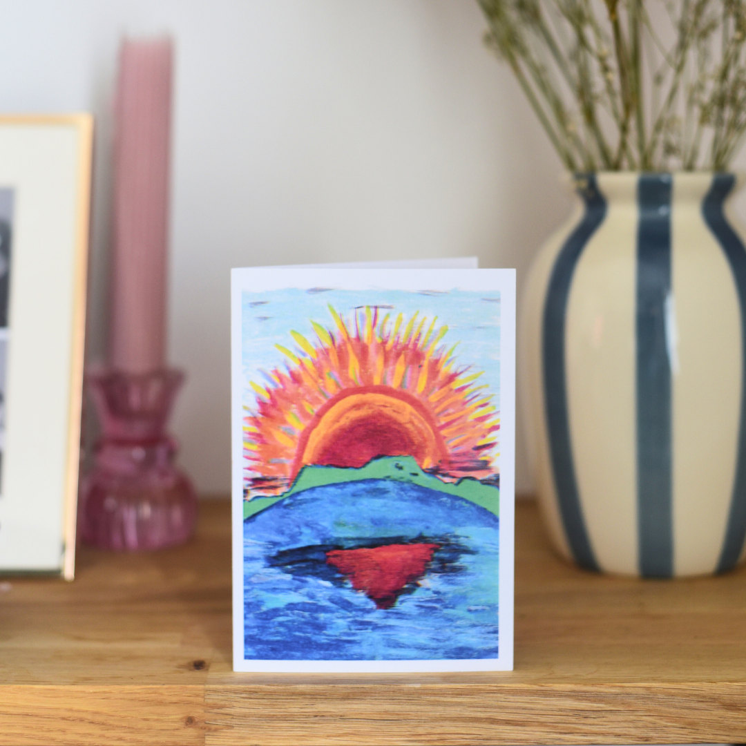 Greeting card with a colorful sunset design on a wooden surface with decor items.